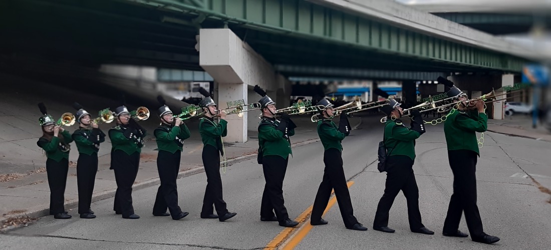 Marching band members in uniform crossing the road while holding their horns recreating the Beatles Abbey Road